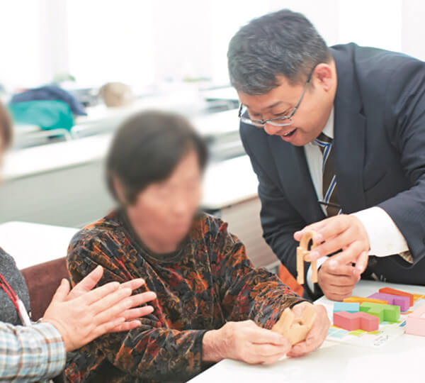 熊本県の「脳いきいき教室」で「パズルで脳トレーニング -ひらめき編-」を楽しむ参加者の皆さん。右は川畑智先生。